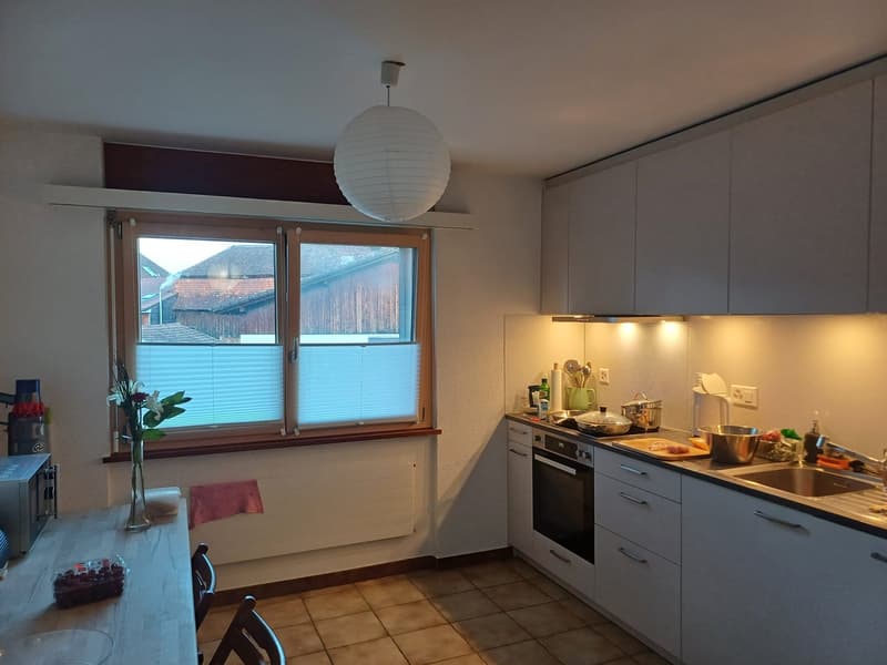 modern kitchen with white cabinets, tiled floor, large window, hanging lamp, sink, oven, microwave, refrigerator, dining table, chairs, flower vase, radiator