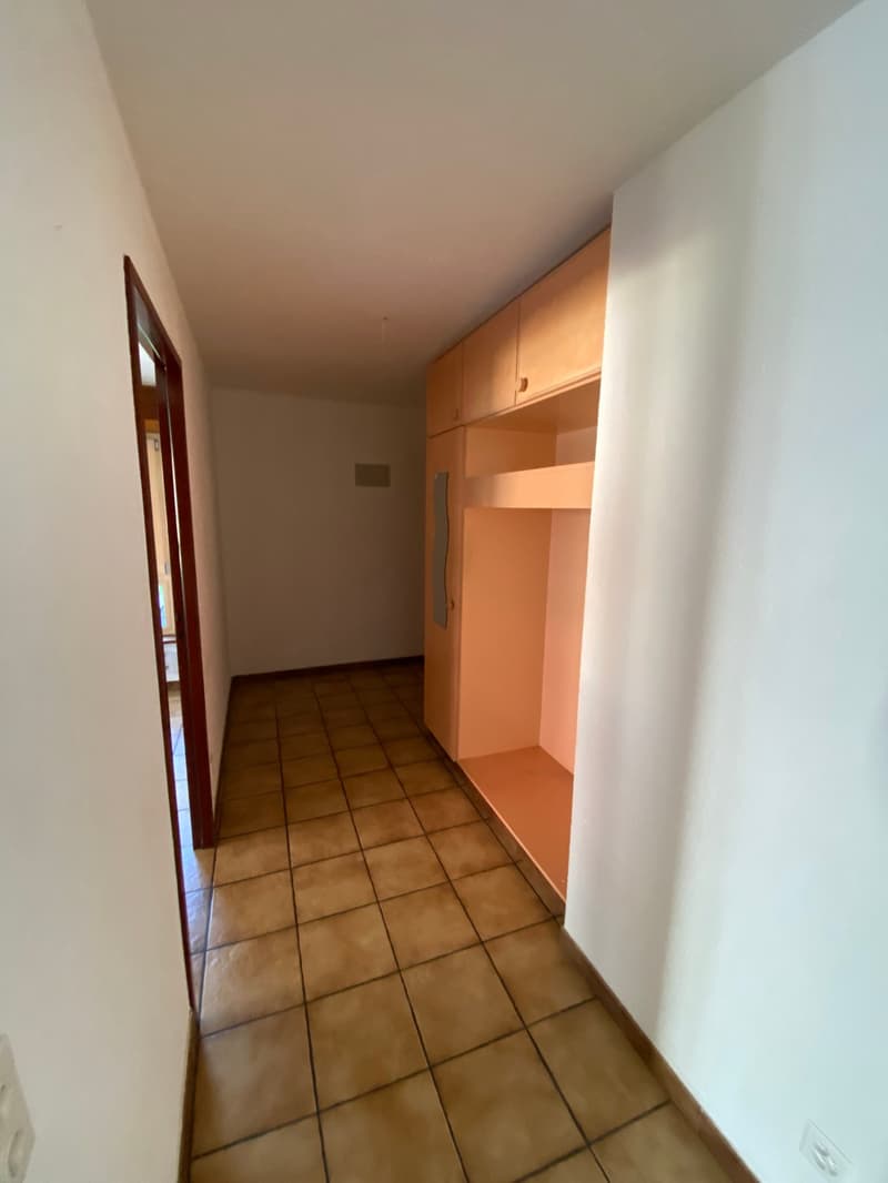 Empty room with tiled floor, white walls, wooden cabinets, and an open door.
