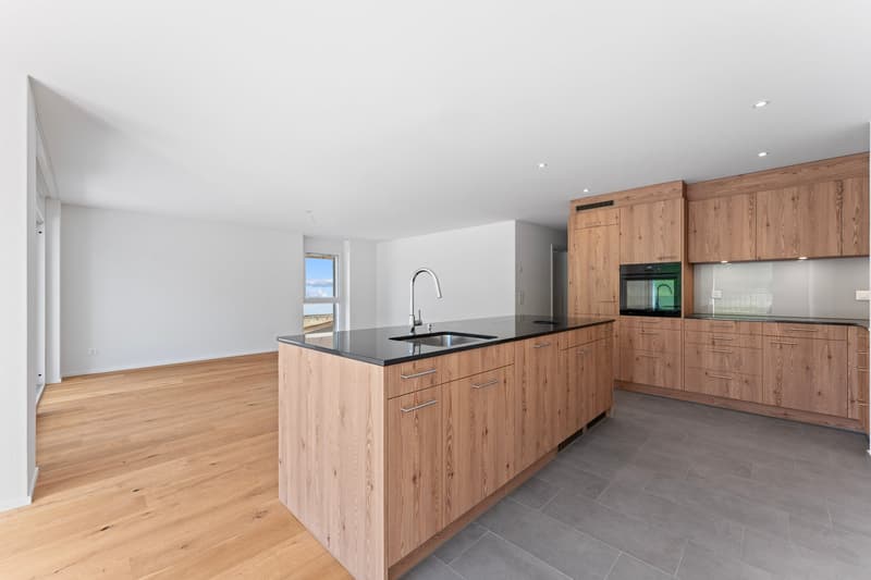 Modern kitchen with wooden cabinets, black countertop, stainless steel sink, oven, and large window.