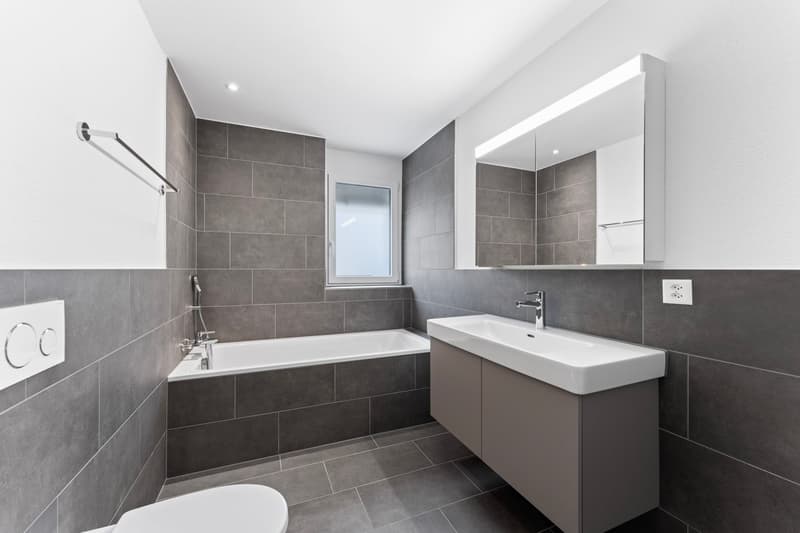 bathroom with bathtub, vanity with sink, mirror, tiled wall, power outlet, light switch