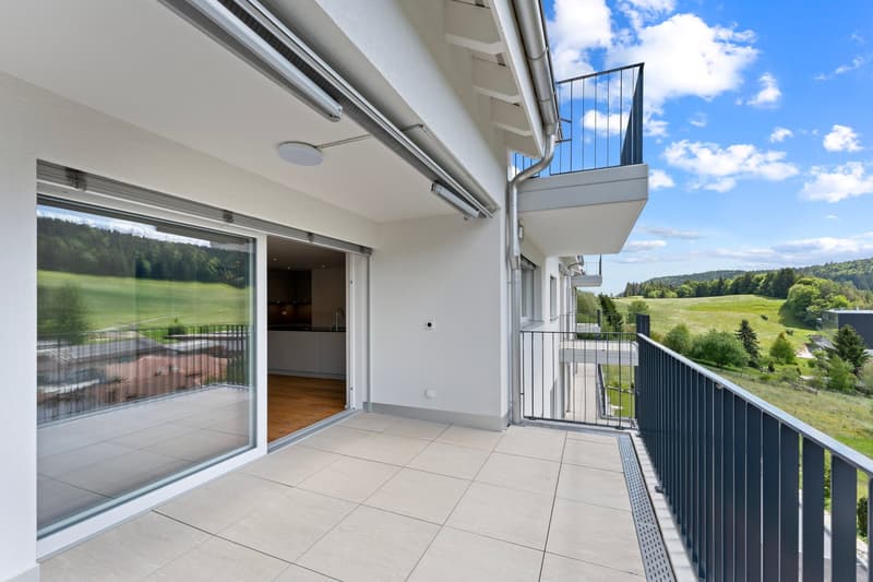 Balcony with tiled floor, glass doors leading to the interior, metallic railings, open view of a green field and mountains