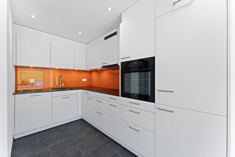 Modern kitchen, white cabinets, black countertops, integrated oven and dishwasher, sleek faucet, tiled floor.