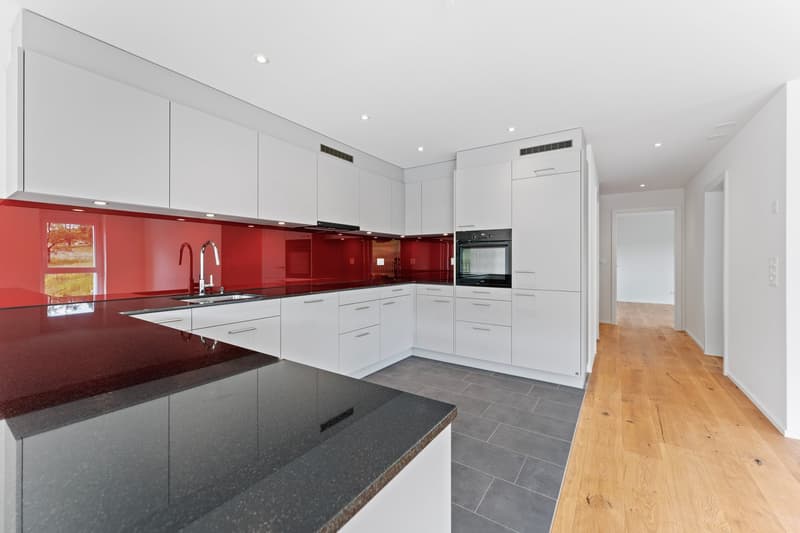 Modern kitchen, white cabinets, red glass backsplash, granite countertop, black kitchen island, built-in oven, built-in microwave, gas stove, double sink, stainless steel faucet