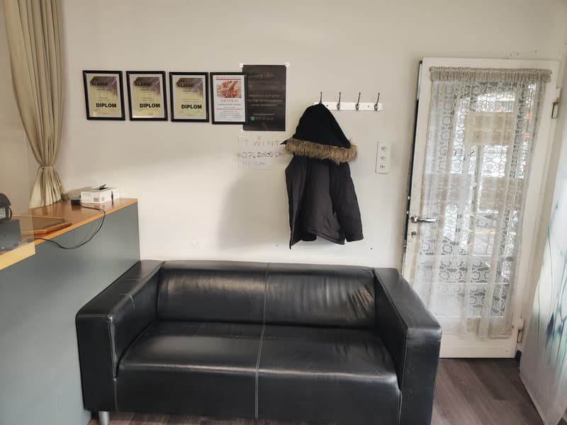Couch, coat hanging on wall, 4 certificates on wall, power outlet, door, table, curtains