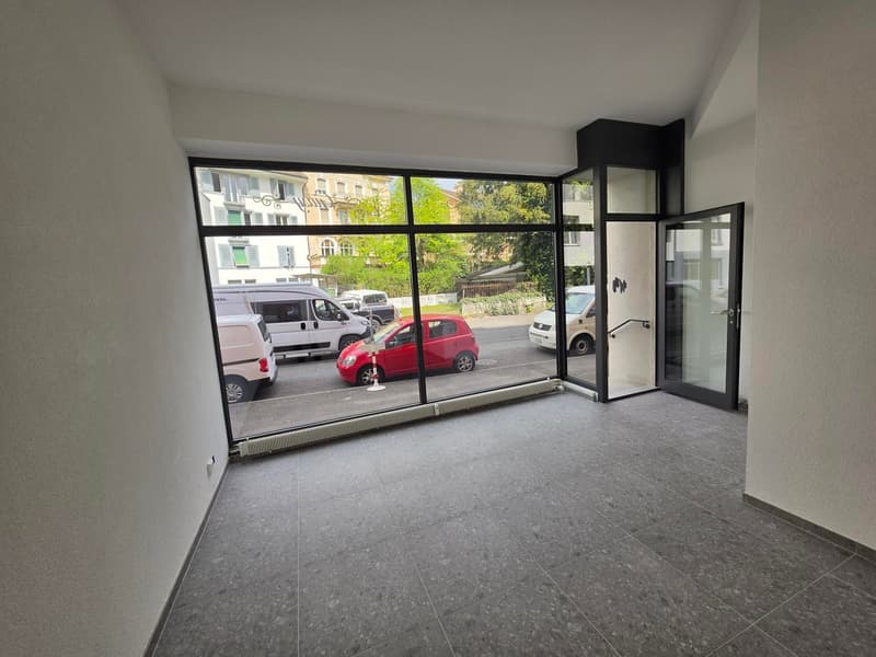 Empty room with large windows, gray tiled floor, white walls, view of street with cars