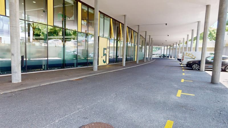Covered walkway with glass walls, concrete floor, yellow parking lines, parked cars