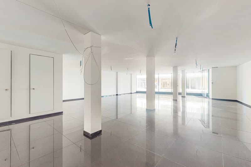 large room with white walls, grey tiles, 4 white pillars, large open windows, and glass doors