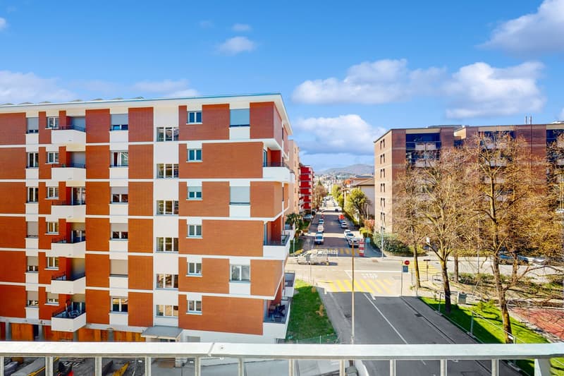 Modern apartment building with orange and white facade, multiple balconies, located in a city with a clear view of the sky and distant mountains