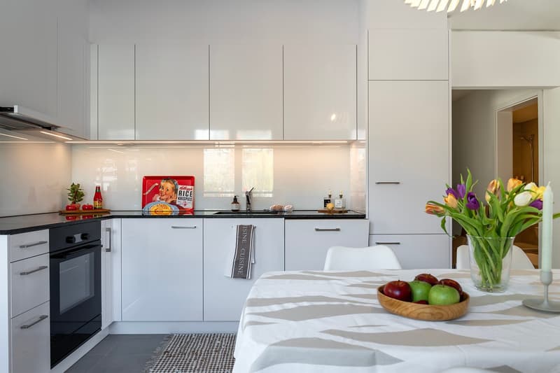 modern kitchen with white cabinets, black countertops, modern appliances, dining table with fruits, flowers in vase