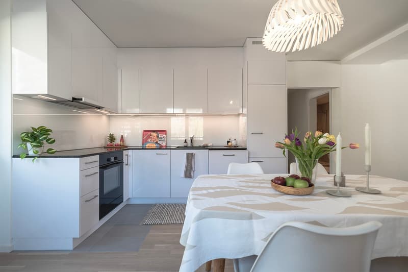 modern kitchen with white cabinets, black countertops, modern appliances, dining table with white tablecloth, flowers, fruits, and candles