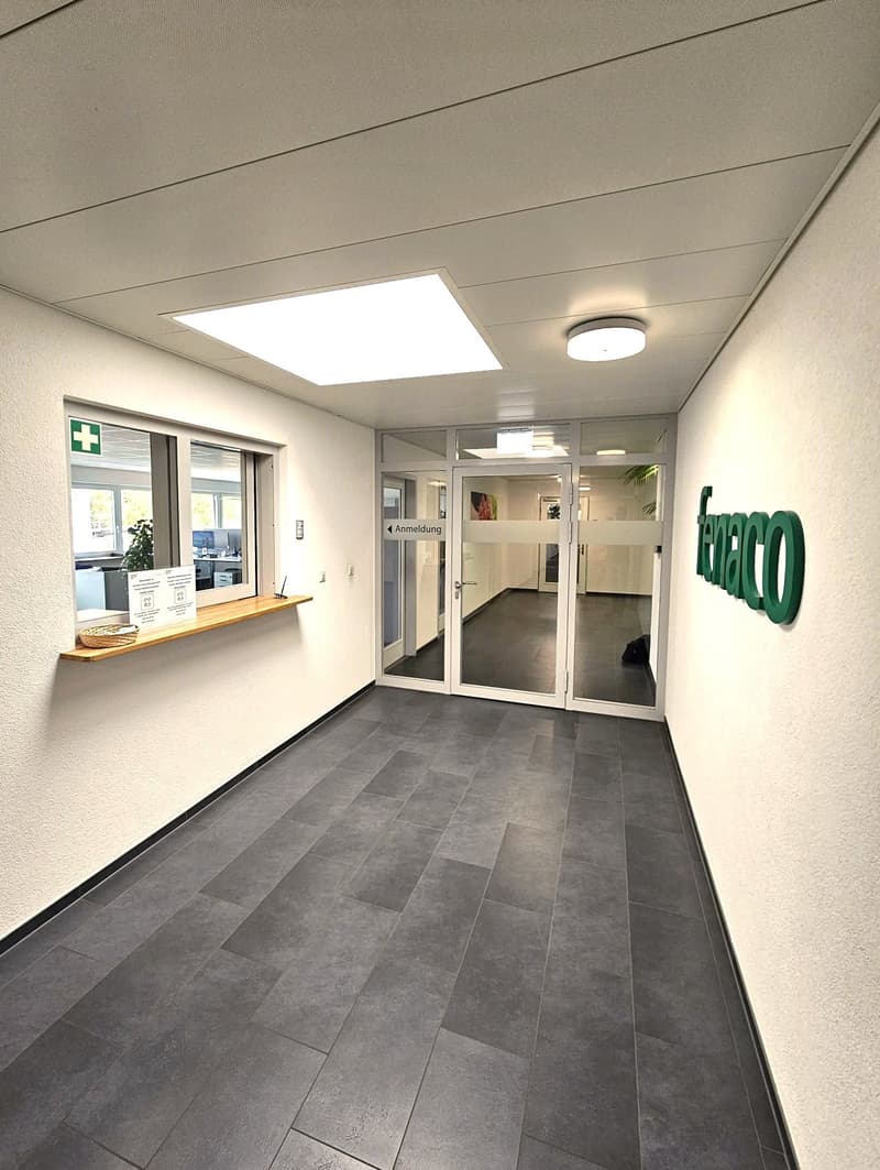 white wall, black tile floor, entrance doors, small window with green cross, ceiling lights