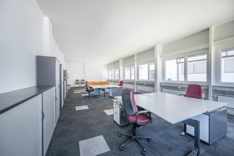 modern office layout with white walls, gray flooring, multiple desks, office chairs, cabinets, large windows