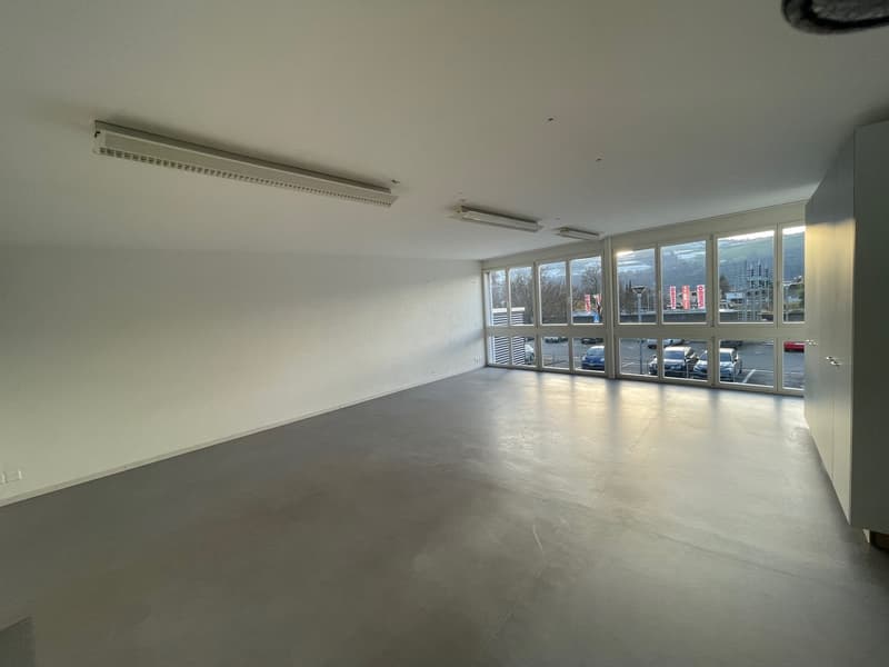 empty room, fluorescent ceiling lights, large windows, concrete floor, parking area view