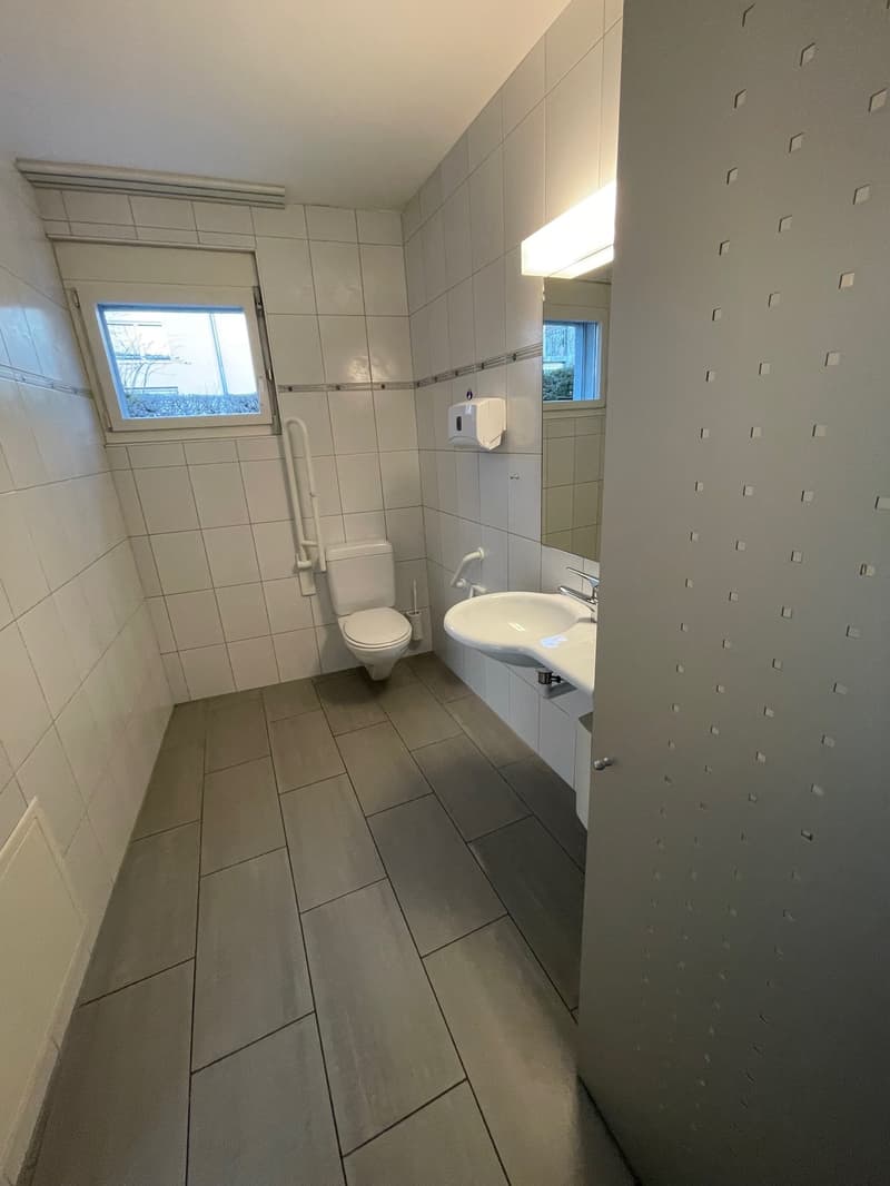 Small bathroom with white tiles, tiled floor, sink, mirror, toilet, and a small window