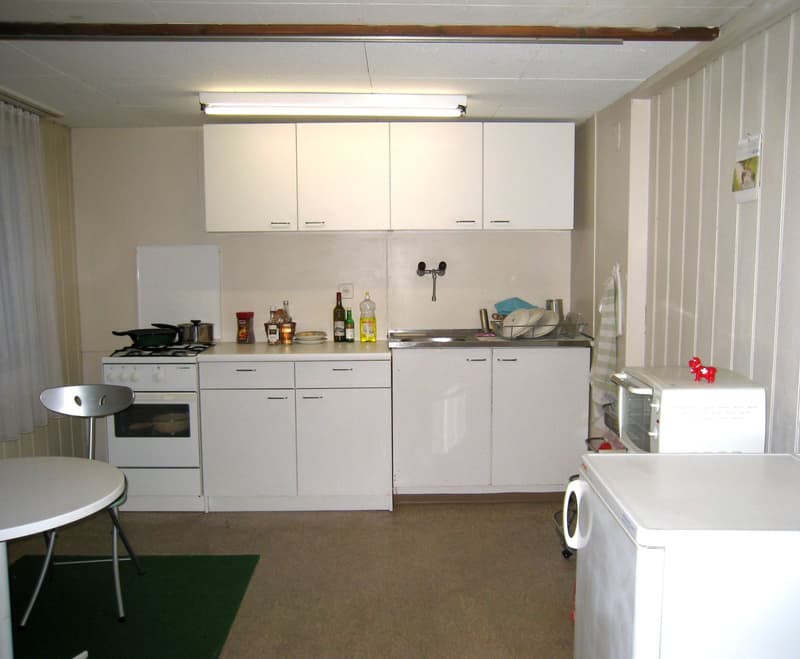 Kitchen with a white color scheme and white appliances, cabinets, gas stove, oven, microwave, fridge, table, and chair.