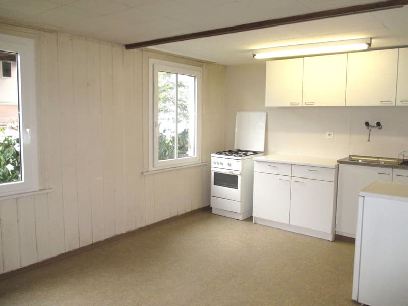 Small kitchen with a white gas stove, white oven, white cupboards, a window overlooking the outside.