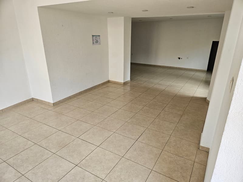 Large open space with beige tile flooring, white walls, and a doorway leading to another room.