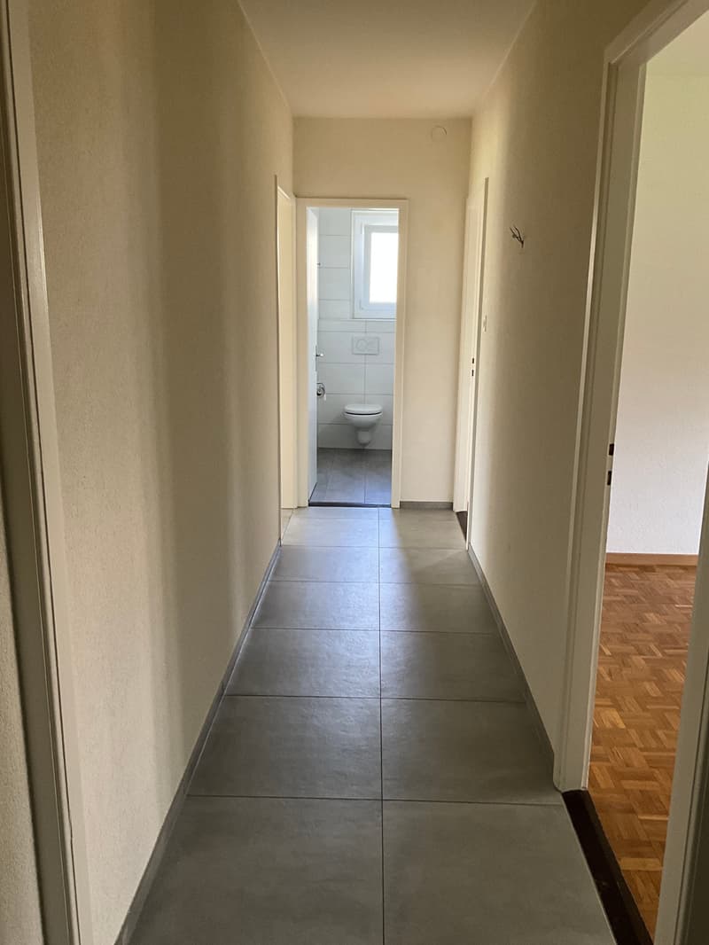 Empty hallway with tiled floor, white walls, and wooden floor in the right corner.