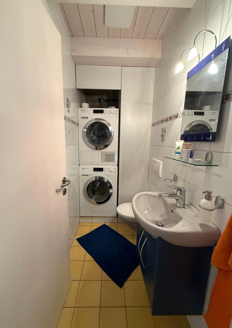 small bathroom with washing machine and sink, mirror, toilet, floor and wall tiles