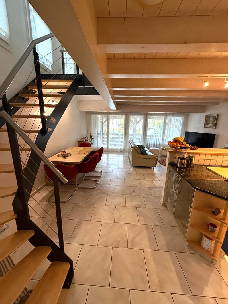 modern design with tile flooring, stairs with metal railing, dining table with red chairs, couch, TV, kitchen island, counter with plates