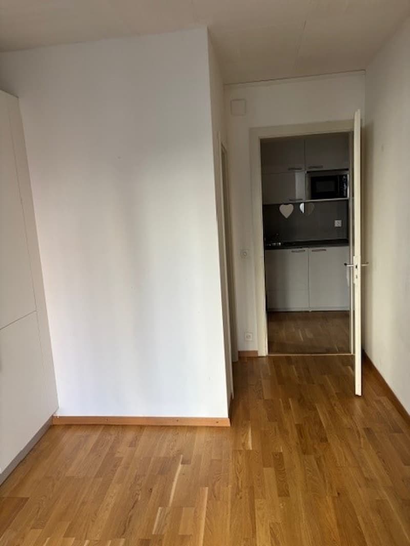 empty room, white walls, wooden floor, white cabinet, open door to the kitchen
