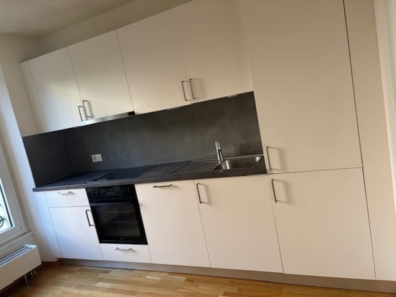 modern kitchen with built-in cabinets, black countertops, stainless steel sink, black stove, white oven, wooden floors, white windows