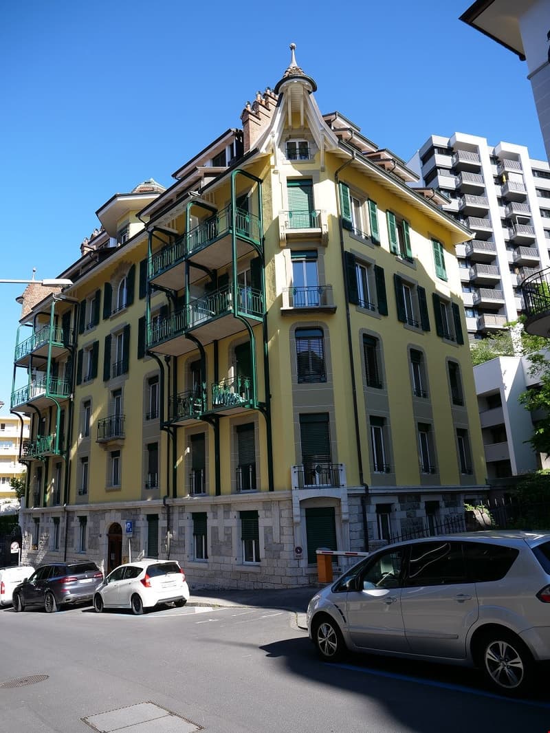 large yellow building with green accents, 4 balconies, multiple cars parked in front