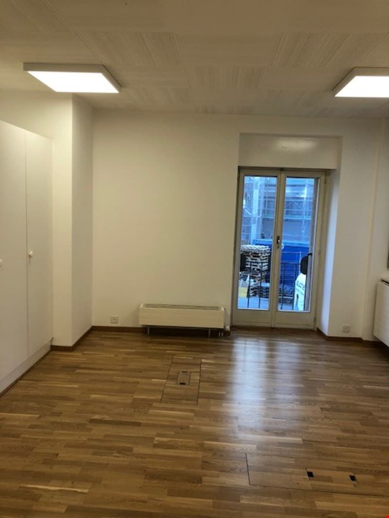 empty room, hardwood floor, white walls, glass doors leading to the outside, white ceiling with recessed lighting, a white radiator