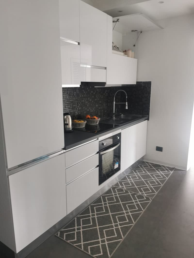 Modern white kitchen cabinets, black countertop, black and white mosaic tile backsplash, built-in oven, dishwasher, fruit bowls on the counter