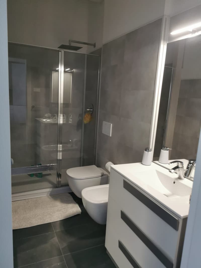 Modern bathroom with glass shower enclosure, white toilet, vanity with sink, and tile flooring.