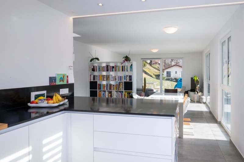 modern kitchen with white cabinets, black countertops, large windows, dining area, bookshelf, plants, view of the outside