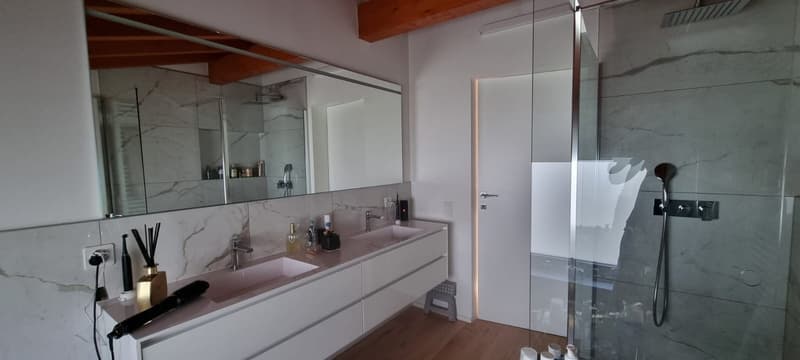 modern bathroom with large mirror, double sink, shower, wooden floor, white walls, marble tiles