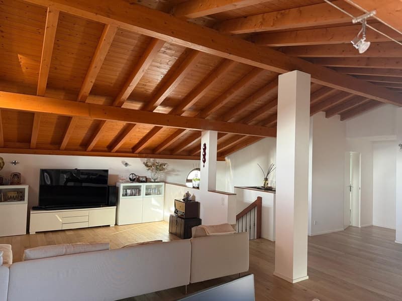 Living room with wooden ceiling, wooden floor, white walls, large sofa, TV, entertainment center, cabinet, staircase, window