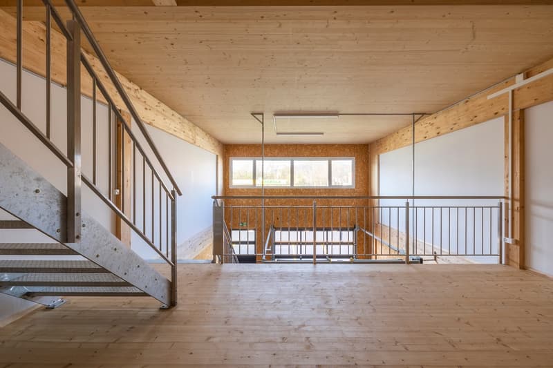 large open space with wooden flooring, metal railing, and glass windows