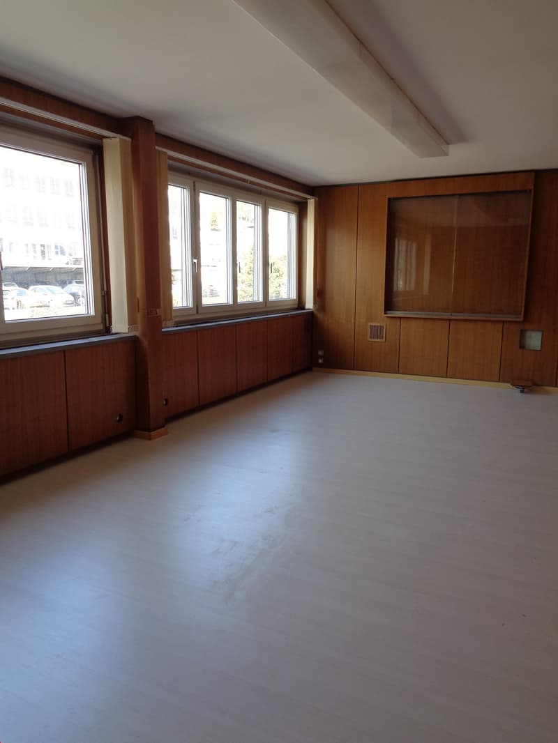 Wooden paneling, large windows, white floor, ceiling light, empty room
