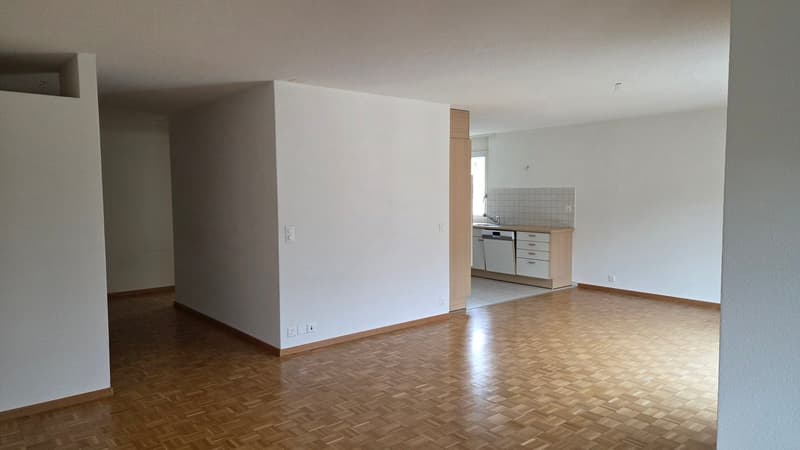 empty room with wooden floor, white walls, kitchen and bathroom visible, power outlets and switches on the walls