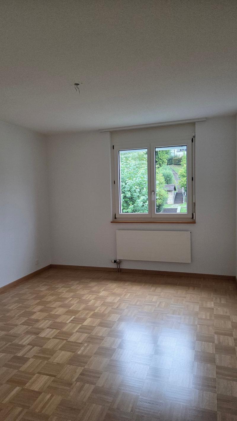an empty room with wooden flooring and a large window providing a view of a hillside