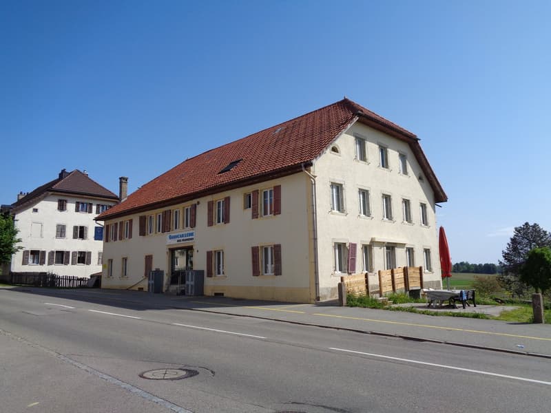 A 2 story house with red tiled roof and beige walls, 10 windows on the second floor, a door with windows, small wooden fences, and a tree in front.