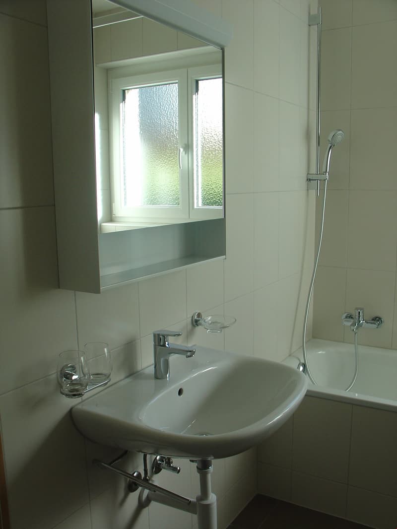modern bathroom with a white tile design, a white sink with a faucet, a glass window, and a shower with a showerhead