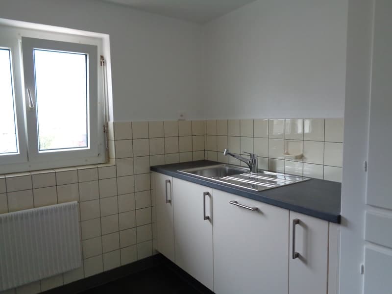 empty kitchen with white tiles, silver sink, cabinets, tiled wall