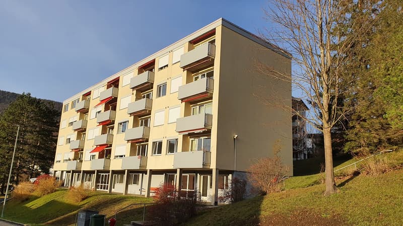 multi-story building, beige exterior, red awnings, balconies, multiple windows, trees, grass