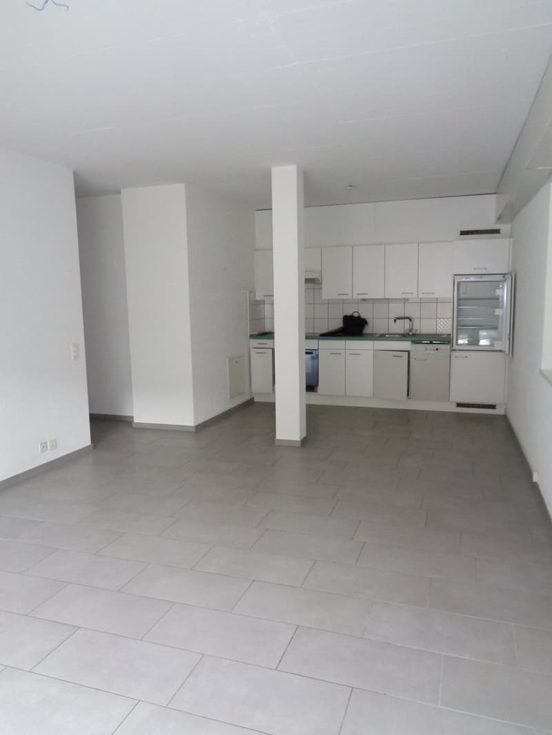 Empty room with white walls, tiled floor, kitchen with white cabinets, sink, and dishwasher