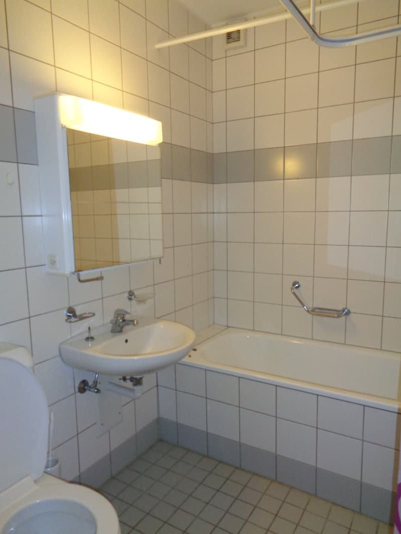 Bathroom with white tiles, white sink, white bathtub, white toilet, mirror, and a shower handle.