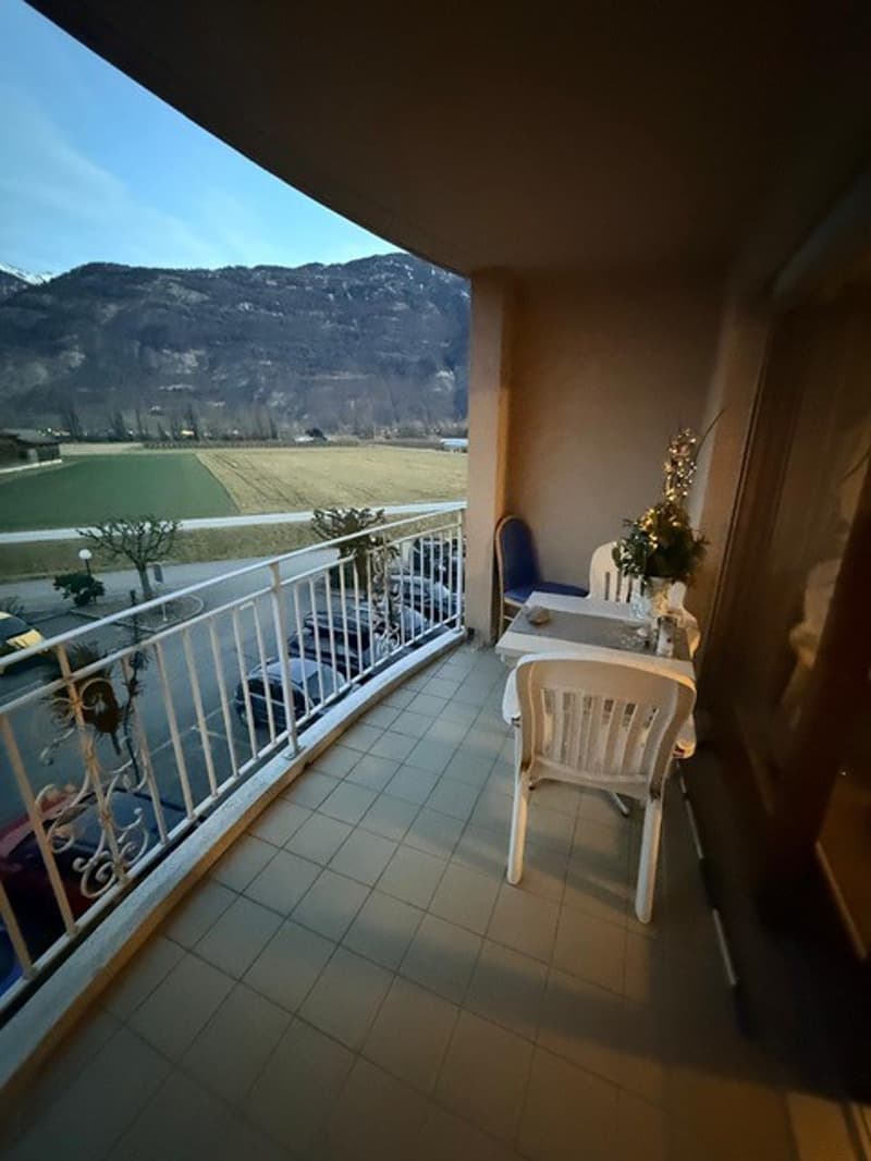 tiled floor, outdoor dining set, metal railing, open view, parked cars, mountain range in distance