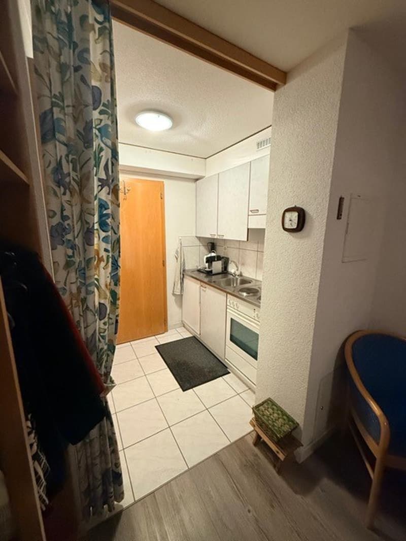 small kitchen, white tiles, white cabinets, stainless steel stove, double sink, wall clock, wooden stool, wooden door, rug