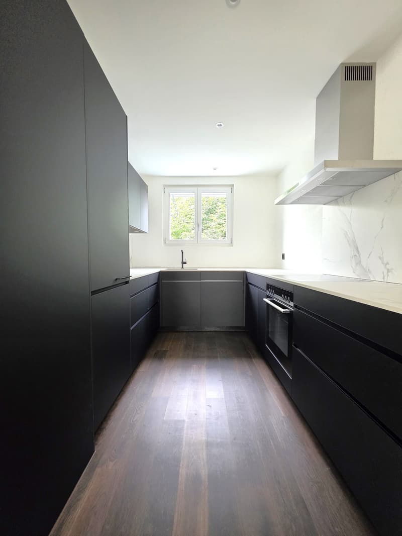 Modern kitchen with black cabinets, white countertops, stainless steel appliances, and a window overlooking the outdoors.