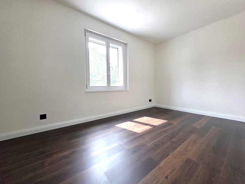 Spacious bedroom with white walls, large windows, and dark hardwood flooring. The room appears to be empty and ready for furnishing.