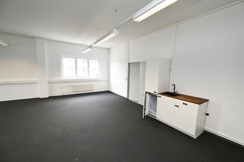 Open space room, a small kitchenette with a sink, small fridge and wooden countertop, two hanging lights