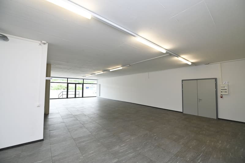 Empty room with white walls, gray tiled floor, and fluorescent ceiling lights.