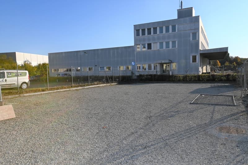 Large building, grey and metal exterior, several windows, small parking lot